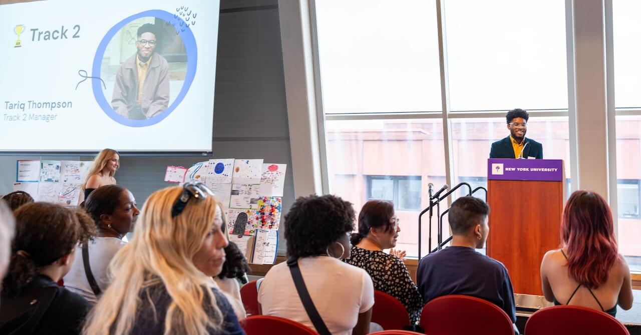 Tariq Thompson at a podium, giving a presentation to an audience of students and families